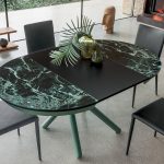 Photo d'une table ronde ouverte avec rallonges noir mat et le plateau en céramique verre brillant effet marbre noir avec des veines vertes.